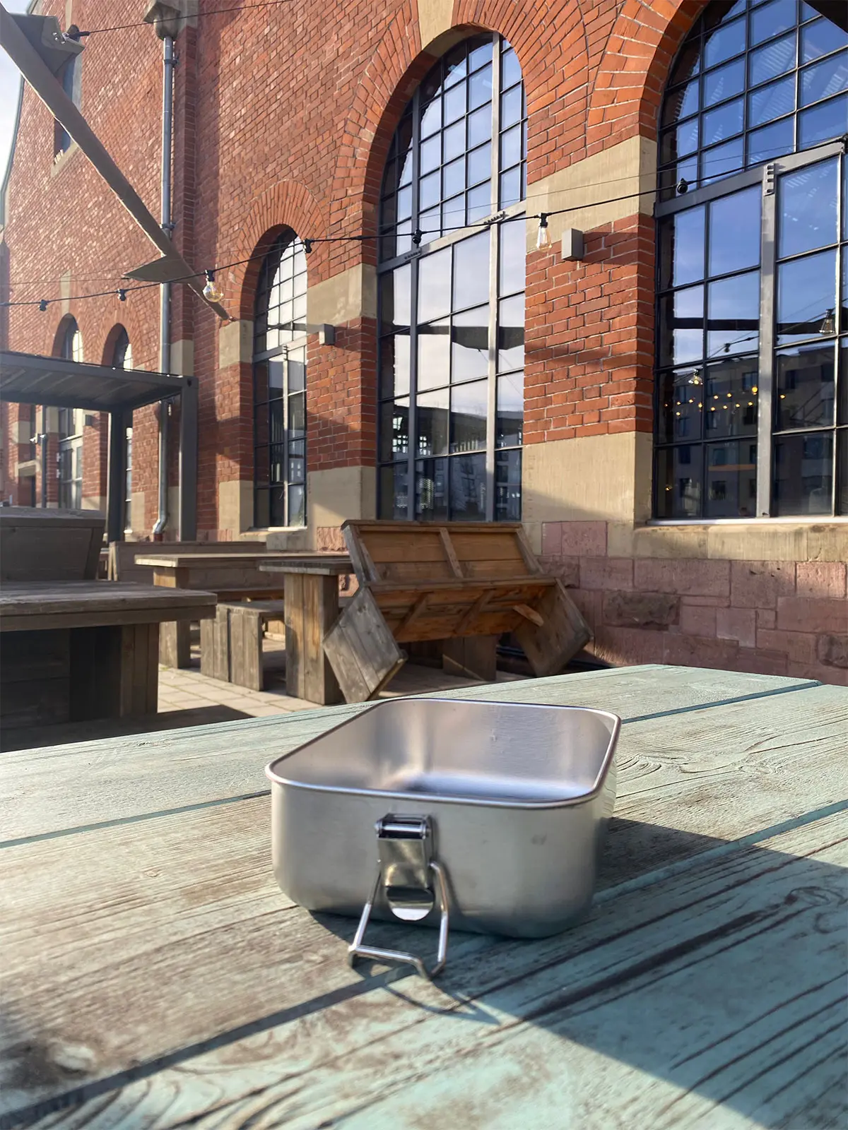 Die Brotdose von HEAT.me steht leer auf einem türkisfarbenem Tisch bei einem alten historischen Gebäude in Freiburg.