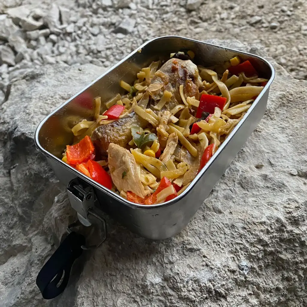 Brotdose mit asiatischen Nudeln, Gemüse und Huhn nach dem Erhitzen mit dem Lunchbox Kit auf einem Felsen
