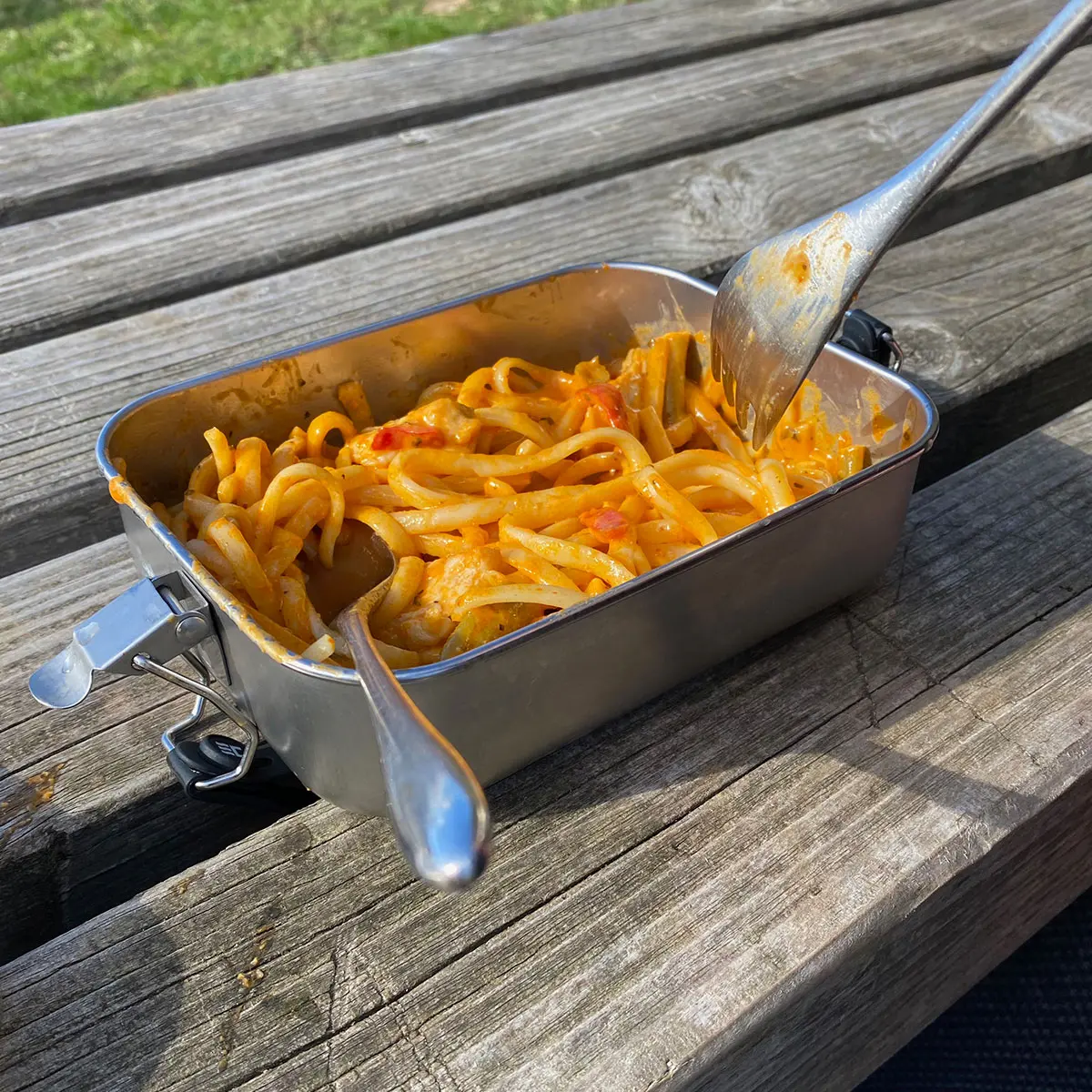 Lunchbox mit Makkaroni und Tomatensause auf einer Holzbank in der Sonne