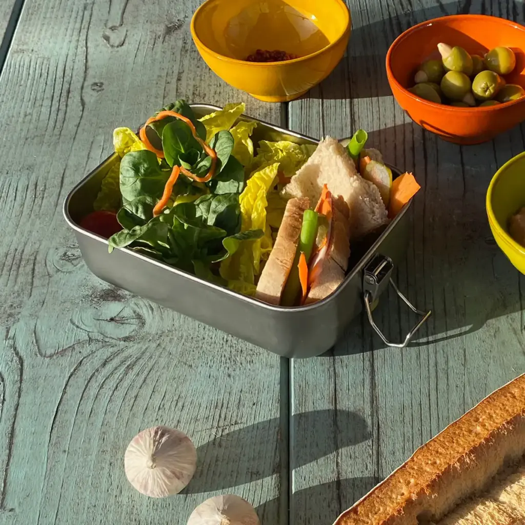 Brotdose gefüllt mit Feldsalat und Sandwiches auf türkisfarbenem Tisch mit Baquette