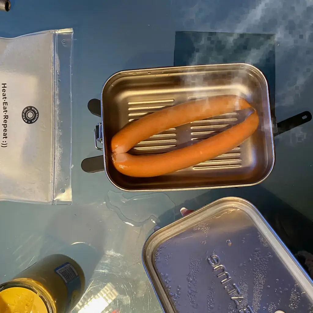 Dampfende heiße Würstchen in der PREMIUM Lunchbox. Daneben ist die HEAT.me Lunchbag zu sehen.