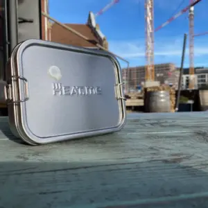 PREMIUM Lunchbox bzw. Brotdose auf grünem Tisch im Querformat. Dahinter sieht man Baustellen