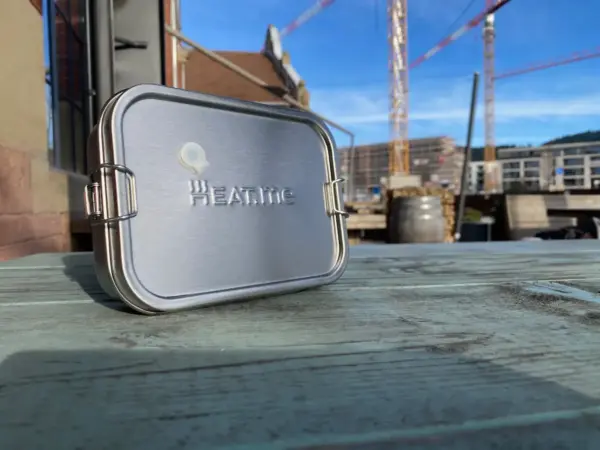 PREMIUM lunch box or lunch box on a green table in landscape format. Behind it you can see building sites