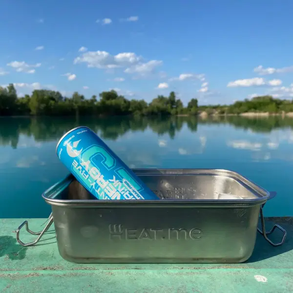 Geöffnete HEAT.me Lunchbox mit Eiswürfel und Slimcan. Im Hintergrund See und blauer Himmel